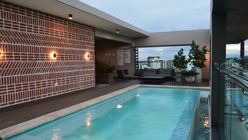 A rooftop pool area with a modern design, including a patterned wall, seating area, and a view of the cityscape.