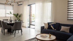Un soggiorno moderno con un divano blu scuro, un tavolino rotondo e una zona pranzo con tavolo e sedie in vetro.
