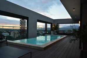 A rooftop infinity pool with a city view, modern architecture, and outdoor seating.