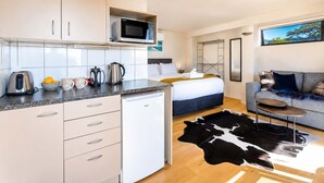 A compact hotel room with a kitchenette, a bed, a sofa, and a large window.