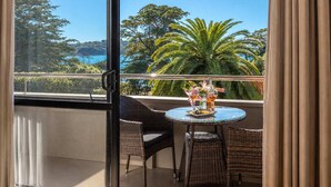 A balcony with wicker furniture, a glass table, and a view of trees and a body of water.