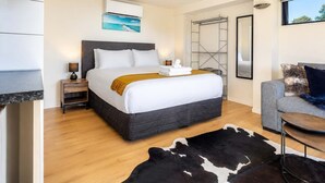 A hotel room with a bed, a small table, a sofa, a cowhide rug, a painting, and a window.