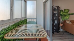 Un balcon avec une porte vitrée, une table en osier, une chaise verte, une plante en pot et un canapé marron.