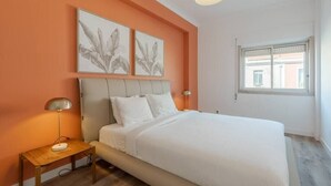 Une chambre à coucher comprenant un lit, une table de chevet, une lampe et deux œuvres d’art accrochées au mur.