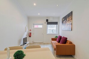 A modern living room with a sofa, a television, a small table, and a window with a view. - Gama Apartment (Setúbal)