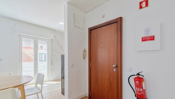 Een kamer met een houten deur, een brandblusser, een tafel met stoelen en uitzicht door een glazen deur.