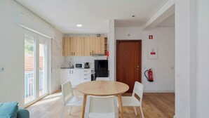 Een moderne keuken met witte kasten, een magnetron en een zwarte koelkast. Er is een eethoek met een ronde tafel en witte stoelen.