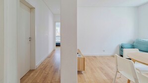 Een modern appartement met een houten vloer, een blauwe bank, een witte eettafel en een deur naar een andere kamer.