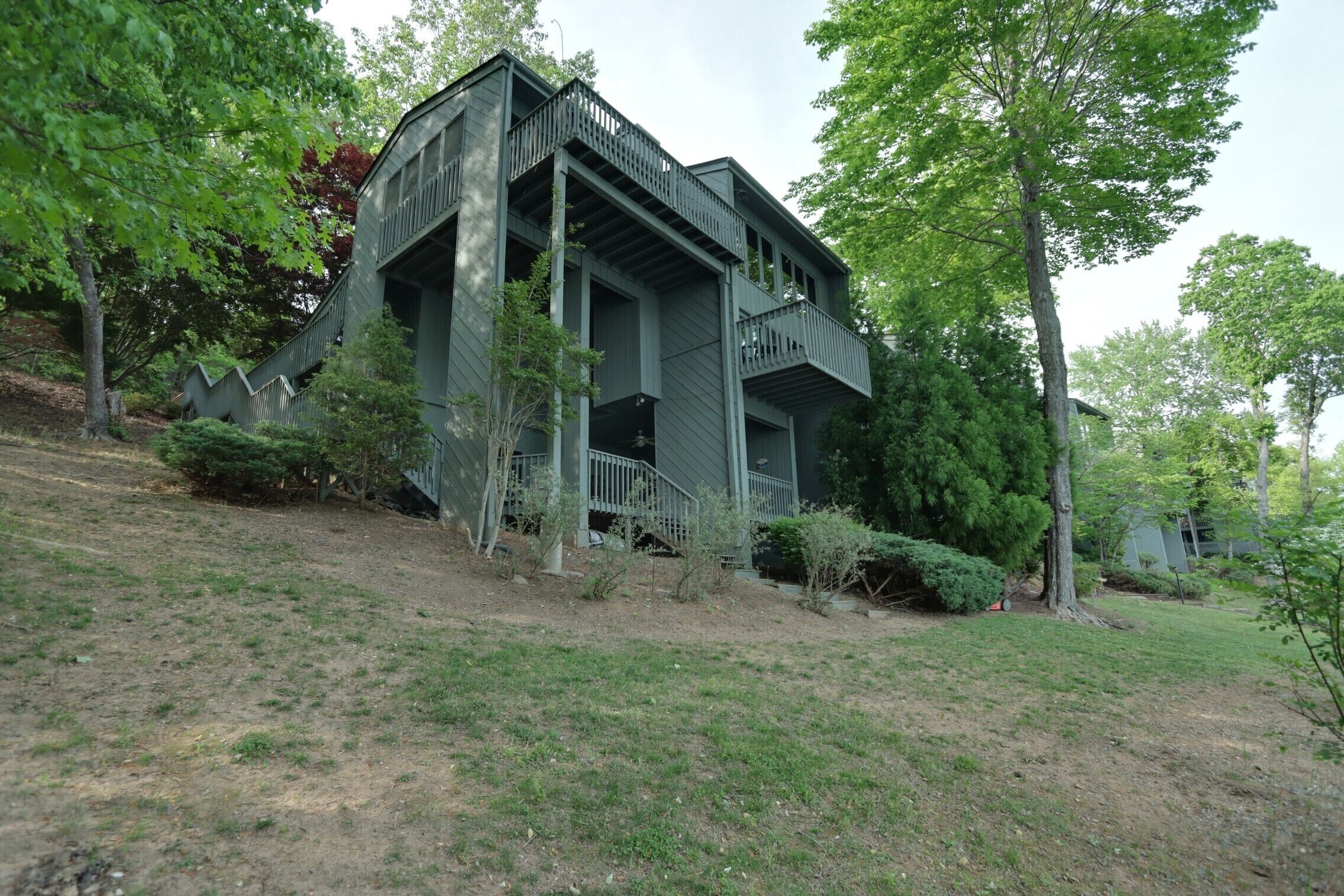 A two-story house with a balcony, surrounded by trees and a grassy yard.