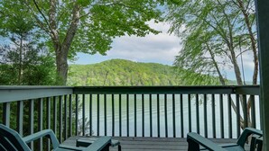 Une terrasse en bois avec deux chaises vertes et une petite table, d’où l’on a vue sur un lac et une colline boisée.