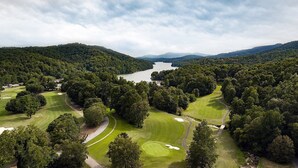 Un parcours de golf avec un lac et des collines boisées en arrière-plan.