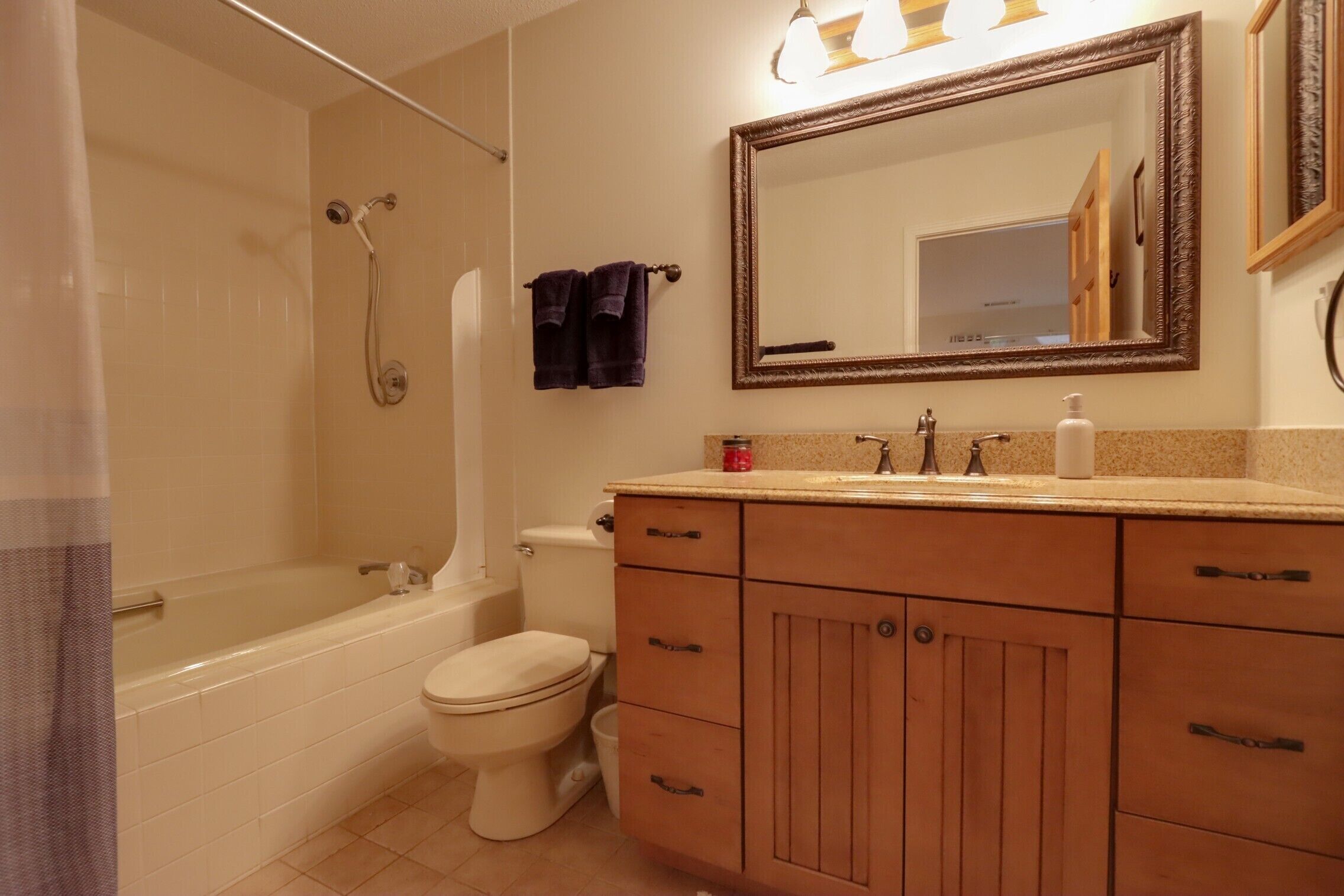 A bathroom with a bathtub, toilet, vanity with drawers, and a mirror.