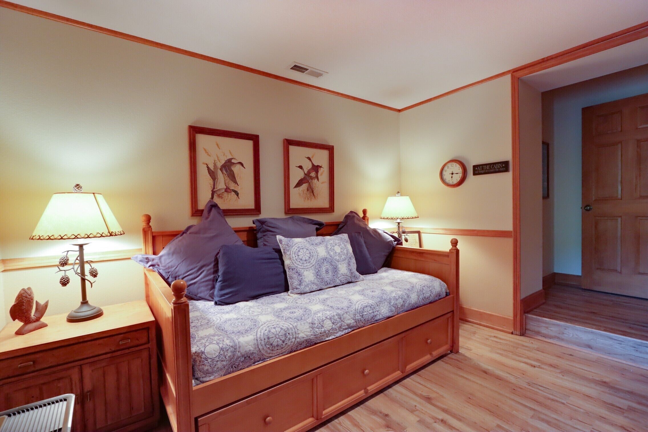 A bedroom with a wooden bed, two wall-mounted lamps, a clock, and framed artwork.