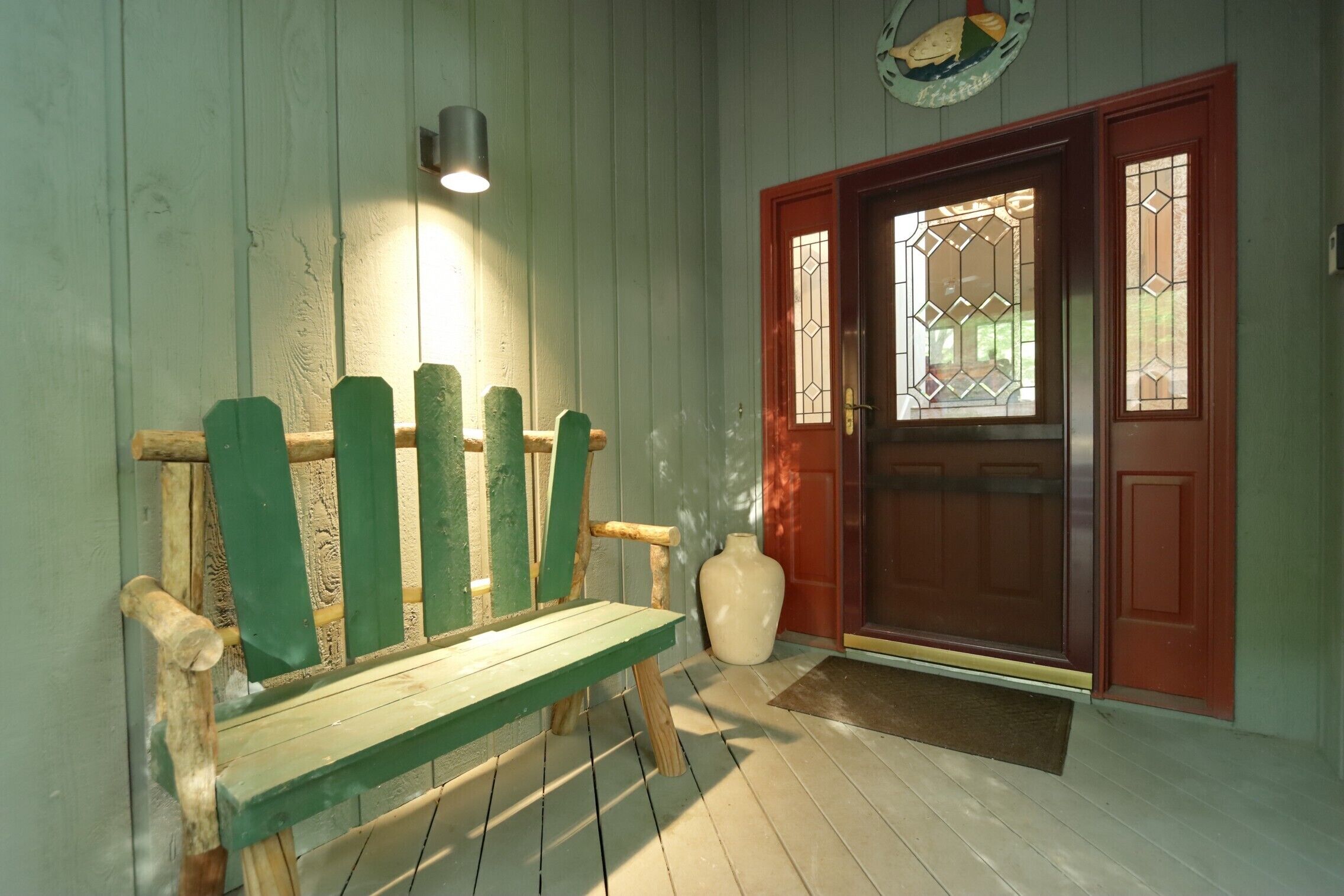 A wooden bench with a backrest, a red door with glass panels, and a wall-mounted light fixture.
