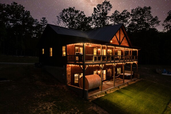 Experience the serene ambiance of this cabin, featuring a balcony with string lights, a well-maintained lawn, and a clear view of the night sky.