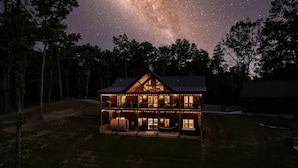Une maison à deux étages, dotée d’un porche avant imposant et d’une grande fenêtre donnant sur un ciel nocturne étoilé.