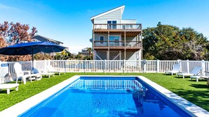 Un edificio de dos pisos con un balcón, una piscina y una valla de piquetes blancos.