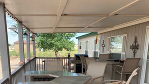 A covered outdoor patio with a glass-top table, wicker chairs, a grill, and a small kitchen area.