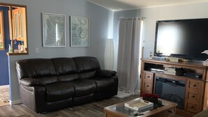 A living room with a black leather sofa, a wooden coffee table, a television, and a cabinet.