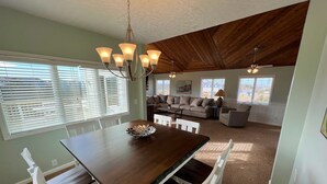 Ein Essbereich mit einem Holztisch und weißen Stühlen, einer Chandelier und Blick auf ein Wohnzimmer mit einer Couch und einer Lampe.