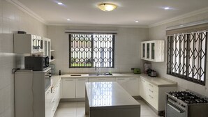 Une cuisine moderne avec des meubles blancs, un îlot central, une cuisinière à gaz et une fenêtre ornée de barreaux décoratifs.