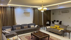 Un salon moderne avec un canapé gris, un canapé plus petit avec des coussins jaunes, une table basse et un lustre.