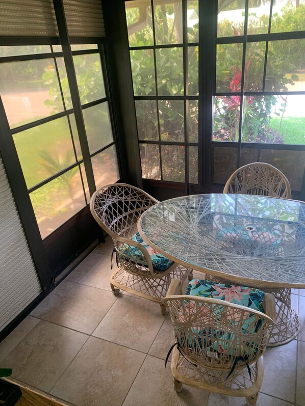 Enjoy a serene view of the garden from this sunroom, featuring a round table and two comfortable chairs.