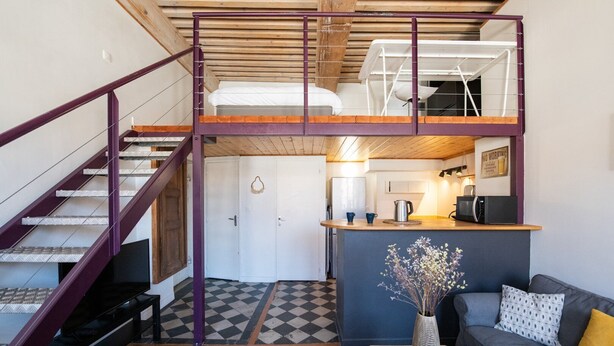 Um espaço de estar estilo loft com escada, cozinha compacta e sofá.