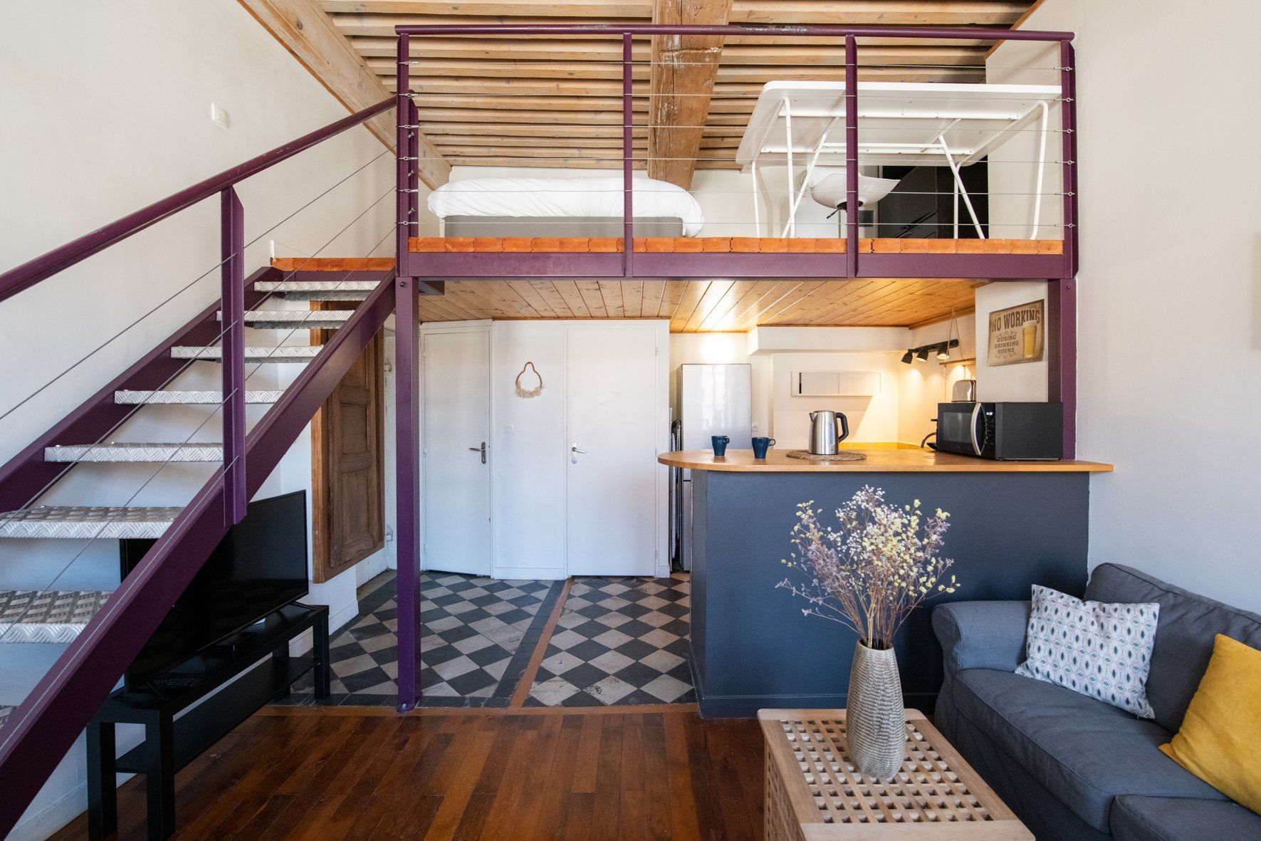 A loft-style living space with a staircase, a kitchenette, and a sofa.