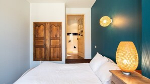 Quarto com guarda-roupa de madeira, luminária na mesa de cabeceira e vista para o banheiro.