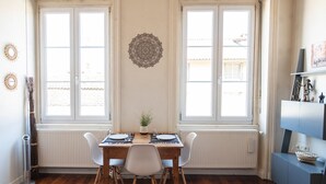 Uma área de refeições com uma mesa de madeira, cadeiras brancas e um vaso com planta.