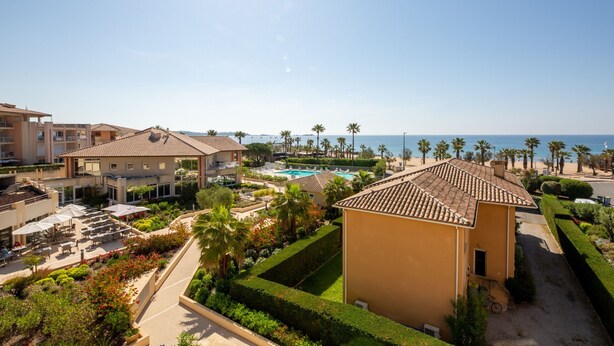 A resort with multiple buildings, a swimming pool, and a view of the sea.