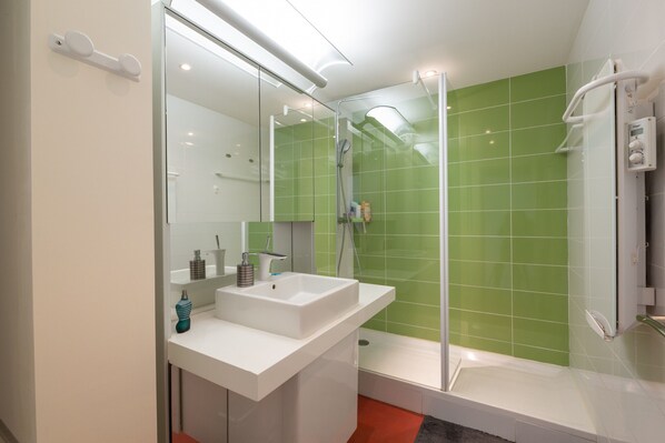 Un baño moderno con ducha de mampara de vidrio, un lavamanos blanco y pared revestida de azulejos verdes.