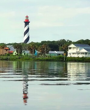 A lighthouse, a body of water, and a white house with a porch.