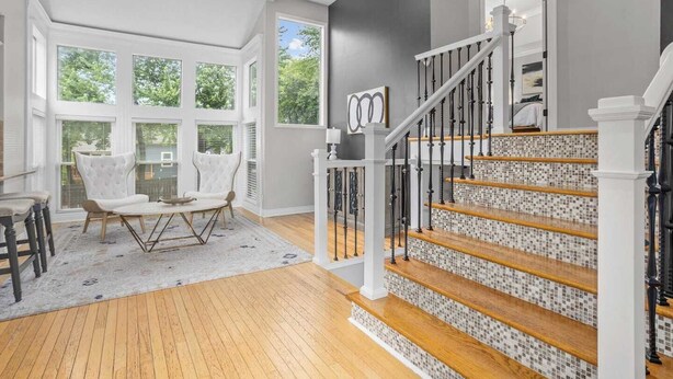 A spacious living room with a large window, a staircase with a mosaic tile design, and a white chair. - Spacious 5-Bed Home with Pool in Overland Par! 27 (Overland Park)