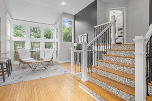 Ein geräumiges Wohnzimmer mit großem Fenster, einer Treppe mit Mosaikfliesen und einem weißen Sessel.
