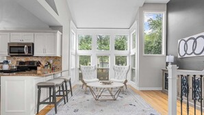 A modern kitchen with white cabinetry, a built-in microwave, and a large window overlooking a garden. - Spacious 5-Bed Home with Pool in Overland Par! 27 (Overland Park)
