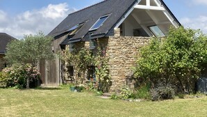 Una casa con fachada de piedra, techo inclinado y un pequeño jardín con diversas plantas y flores.