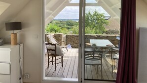 Una habitación con puerta corrediza de vidrio que da a una terraza exterior con mesa y sillas, una lámpara y un muro de piedra.