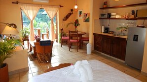 A hotel room with a bed, a dining area with a table and chairs, a kitchen with a refrigerator and a sink, and a ceiling fan. - WATER VIEWS! Luxury Boho In-Village Apt #3 (Boca de Tomatlán)