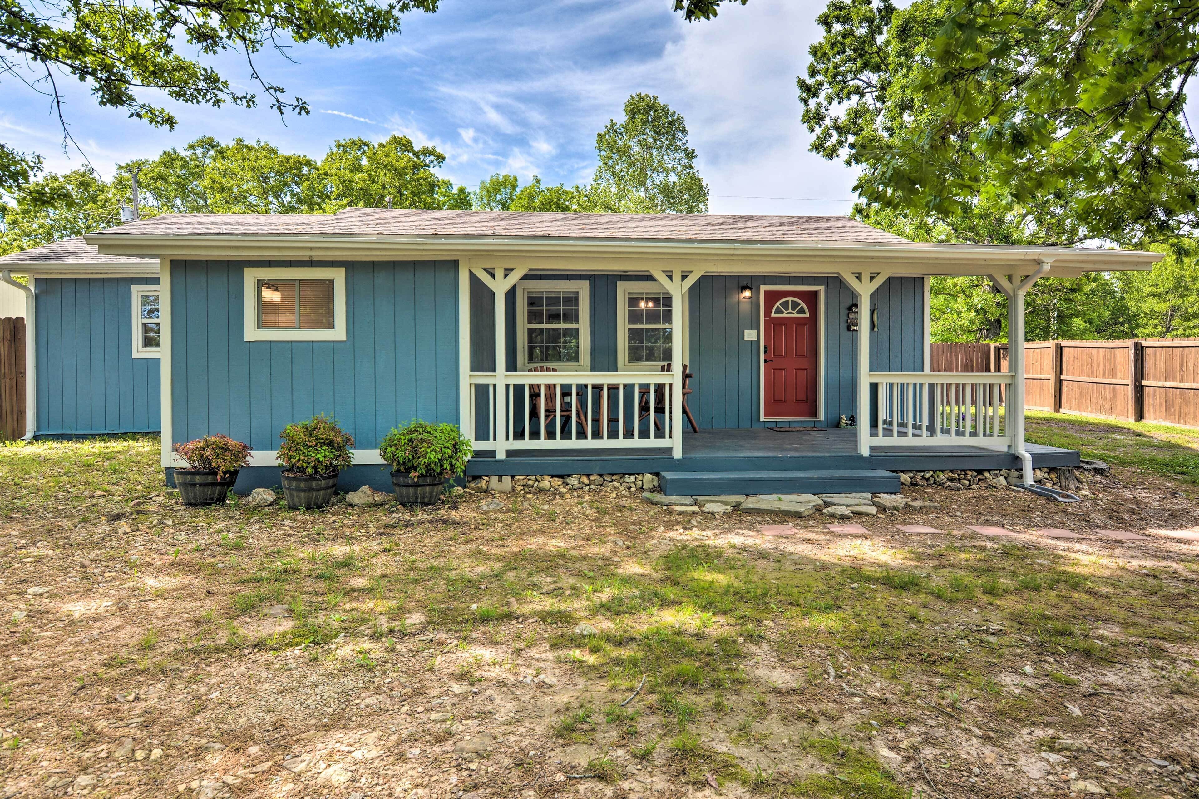 A single-story house with a porch, a red door, and a small front yard with potted plants.