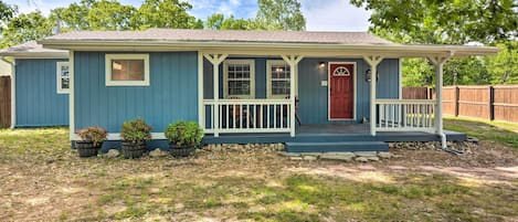 A single-story house with a porch, a red door, and a small front yard with potted plants.