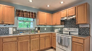 A kitchen with wooden cabinets, a tiled backsplash, a window with a view, and a stove. - Table Rock Lake Retreat < 1 Mi to Boat Launch (Golden)