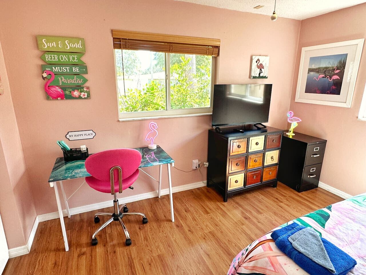 A bedroom with a desk, chair, dresser, TV, and artwork.