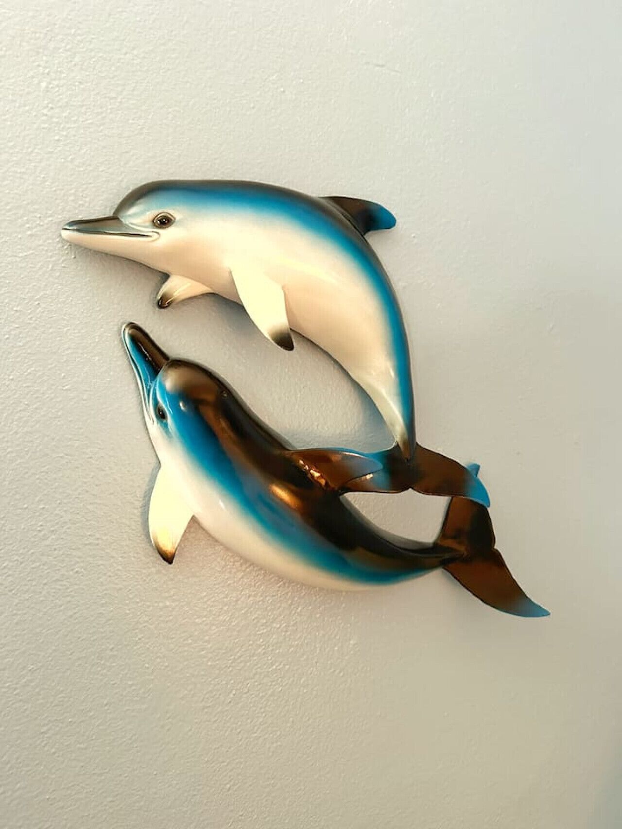 Two dolphin wall art pieces on a plain wall.