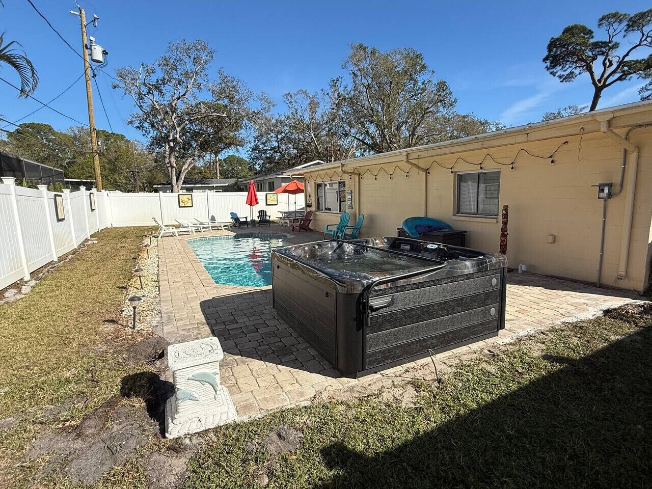 Un patio trasero con jacuzzi, piscina y zona vallada.