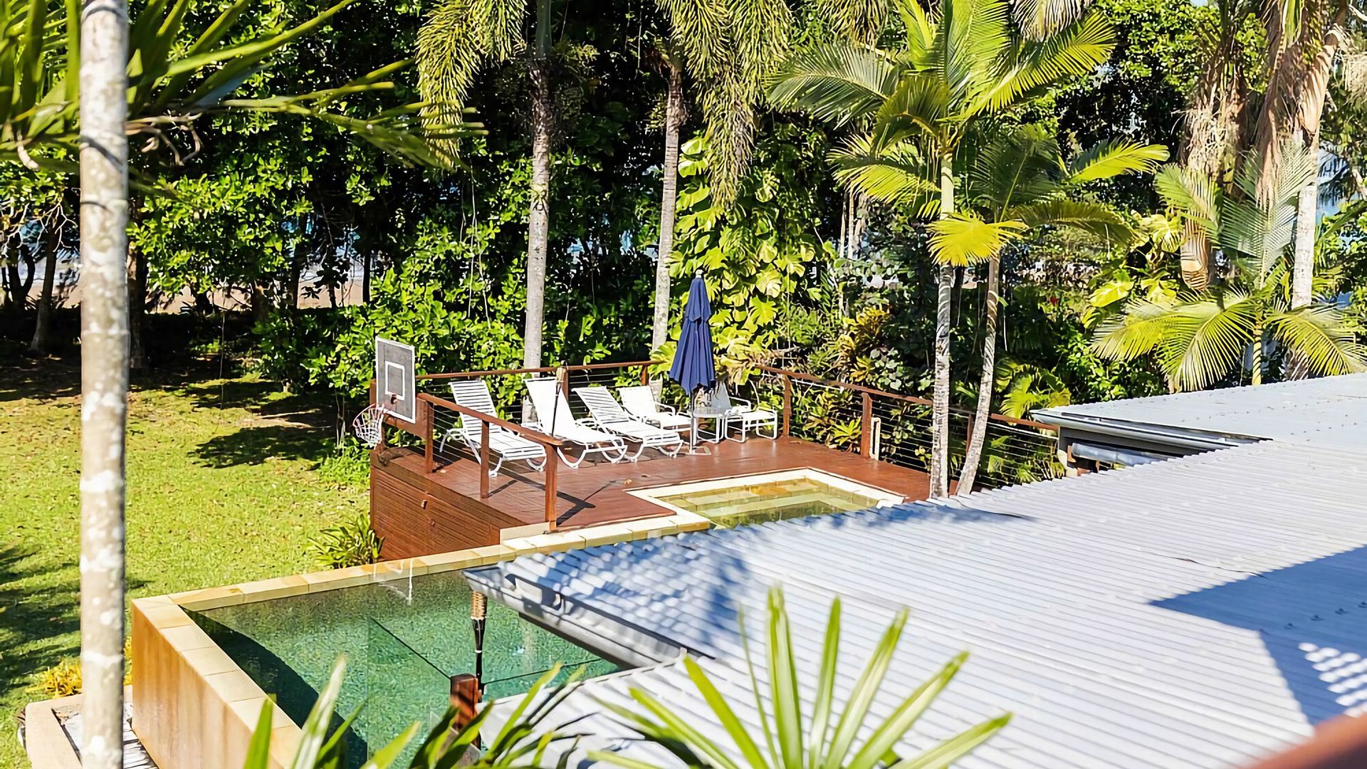 A pool area with a basketball hoop, lounge chairs, and a wooden deck.