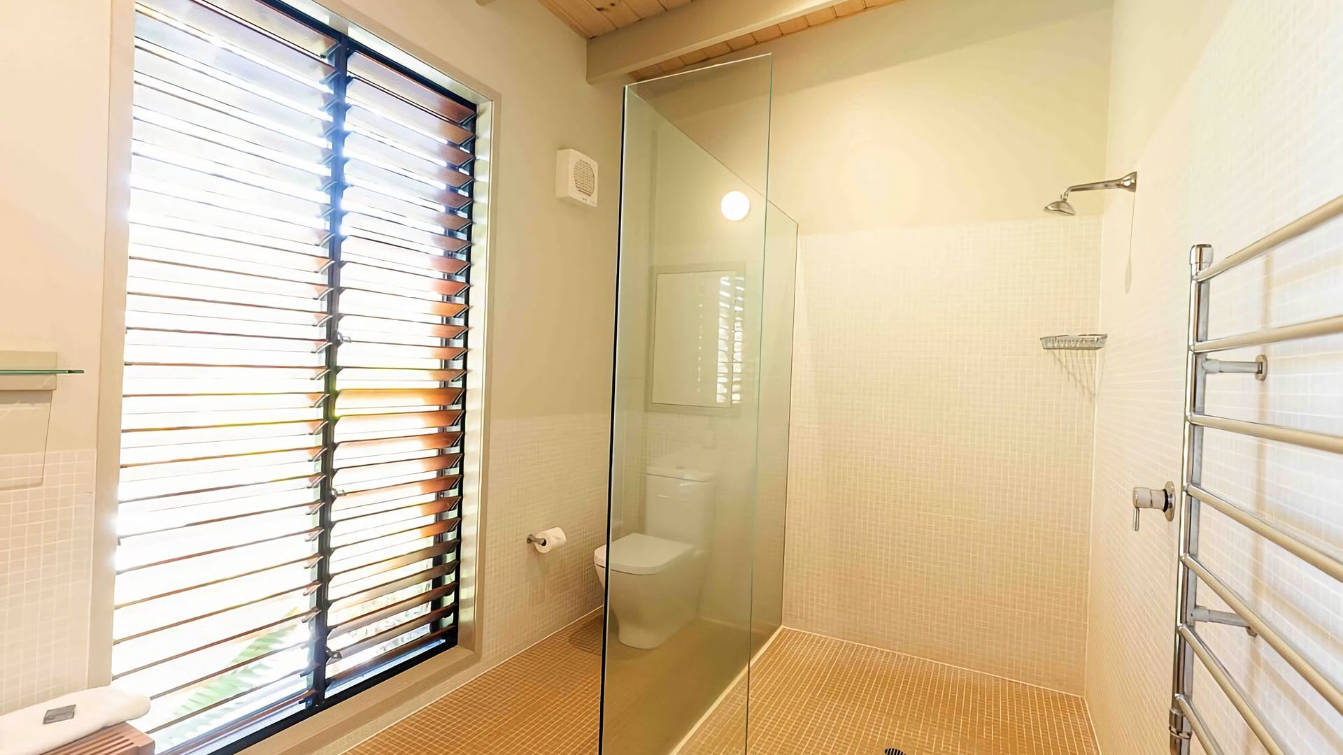 Un baño con cabina de ducha de vidrio, inodoro y ventana con persianas.