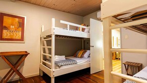 Una camera con un letto a castello, pavimento in legno, un tavolino e un quadro appeso al muro.