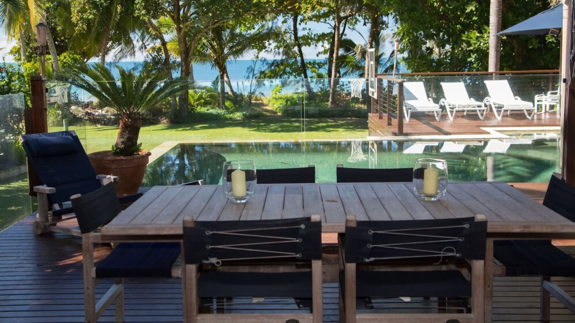 A wooden deck with a table and chairs, overlooking a pool and a view of the ocean.